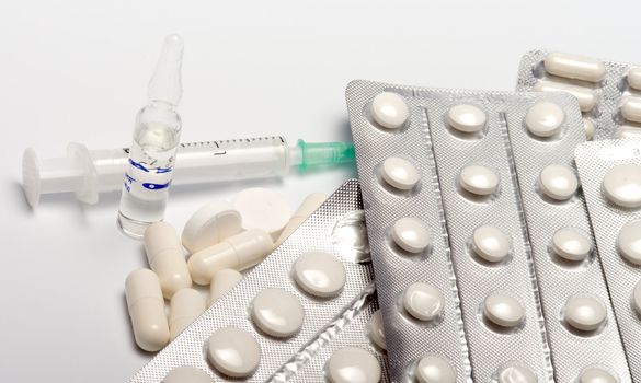 Tablets in packings of a capsule a syringe and an ampoule on a white background.