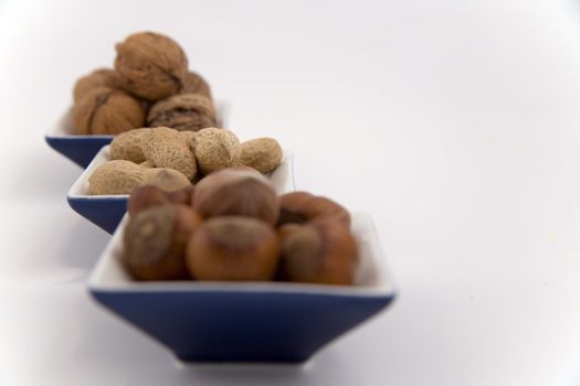 walnuts, hazelnuts and peanuts in three bowls on white background