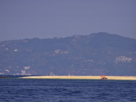 Red umbrella at sandy beach with clear blue sea in front.