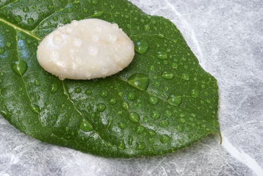 Some fresh water sprinkled over a stone and a leaf which is on a marble background.
