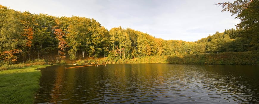 panorama of autumn trees behind a pond