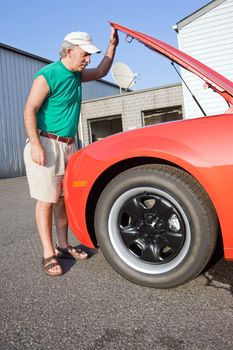 A middle aged man looking under the hood of a car.