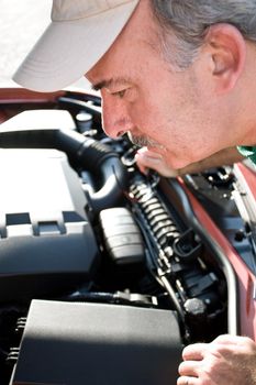 A middle aged man looking under the hood of a car.