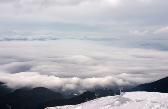 Ski lift in clouds with forest and snow