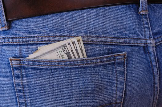 Several 5 dollar bills poke out of the rear pocket of someone's jeans. A temptation for a pickpocket.