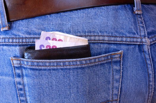 A wallet with several 20 pound bills in it pokes out of the rear pocket of someone's jeans. A temptation for a pickpocket.