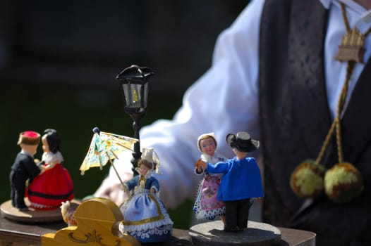 Little dolls dance on top of a barrel organ as the organ grinder (in the background, wearing a pom-pom tie) plays his music. The little woman doll has a wonderfully blas� expression on her face. Space for text.