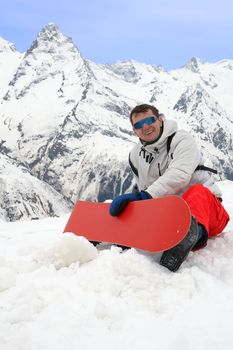 Happy man with red snowboard in mountains