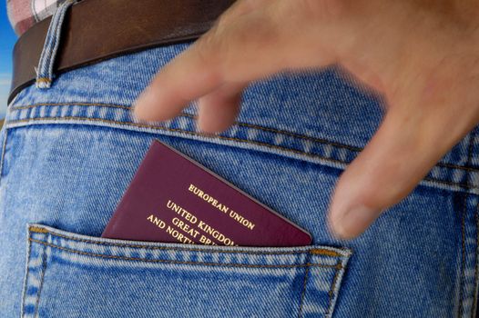 An EU passport pokes out of the rear pocket of a traveller's jeans. Motion blur on a pickpocket's hand, about to take it.