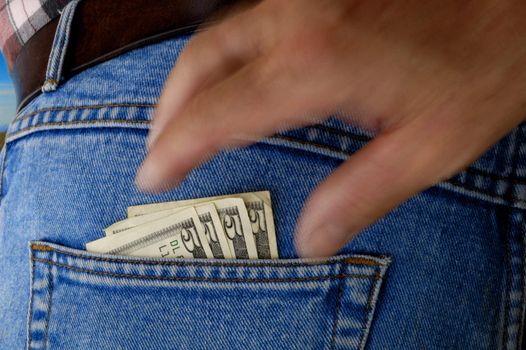 A bunch of 5 dollar bills poke out of the rear pocket of a traveller's jeans. Motion blur on a pickpocket's hand, about to take them.