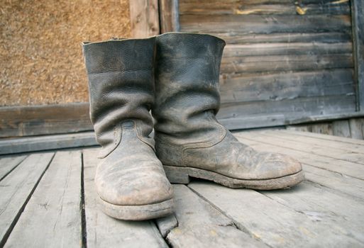 old muddy farmers boots on background wooden wall