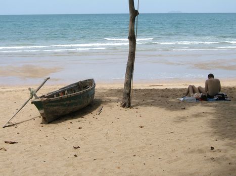 A couple on the beach with the sea, sand and old wooden boat