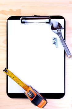 Office accessories for information preservation: Blank Clipboard for the worker with tape measure, wrench and bolt.