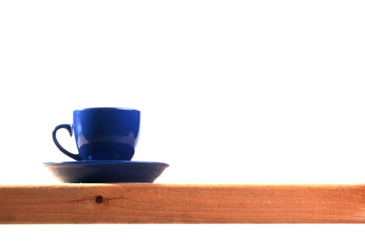Dark blue tea cup with a saucer on a wooden shelf.