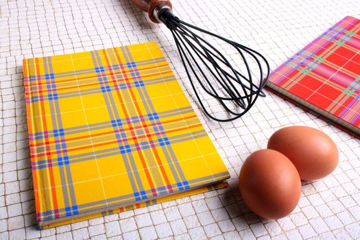 Two books for recipes on a kitchen table with eggs and a beater.
