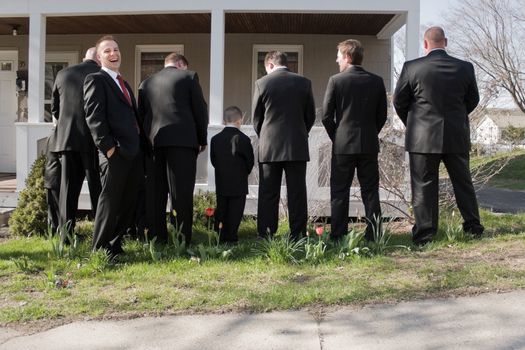 The groomsmen and other male members of a bridal party peeing in the bushes while the groom laughs.