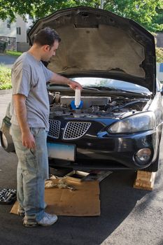 A young man adding oil to his car at the end of an oil change.