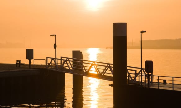 Silhouette of harbor with misty sunrise above the river in late summer