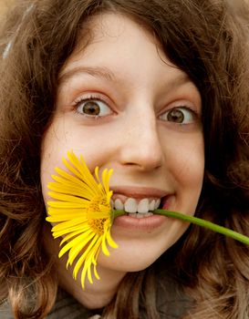 Portrait of the cheerful girl with the big yellow camomile in a teeth 
