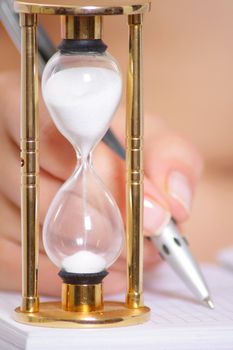 Female hand with pen and sand clock removed close up