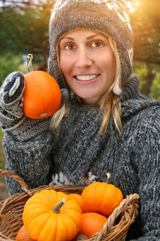 Pretty young woman holding basket full of small pumpkins