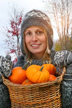 Young woman holding a basket full of small pumpkins
