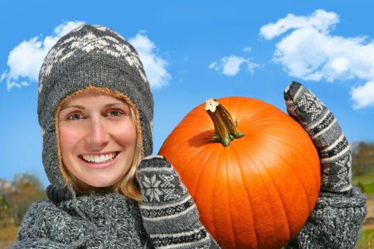 Young woman holding up a big pumpkin against a blue sky