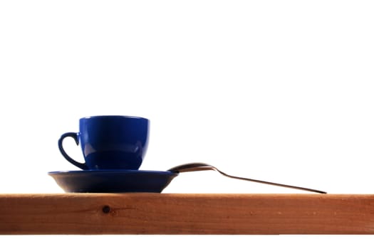 Dark blue tea cup with a saucer and spoon on a wooden shelf.