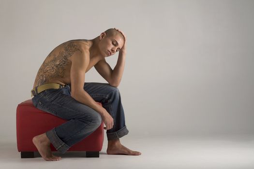 A young, muscular brazilian man in a studio shot, on a red seat, on a gray background.