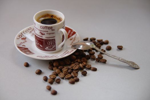 Cup of coffee with saucer, spoon and some coffe beans