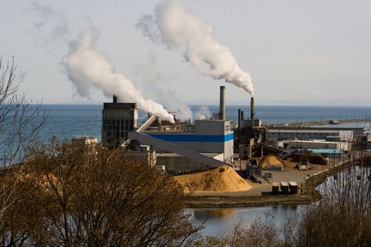 Paper mill manufacturing plant with smoke or steam coming from the smokestacks near Port Angeles, Washington next to the ocean of the Puget Sound with Mt. Baker on the distant horizon. 