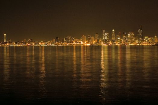 Seattle Skyline with Space Needle with Night Lights across the waters of the Puget Sound. The buildings and waters are lit up in the skyscrapers on this picturesque background.