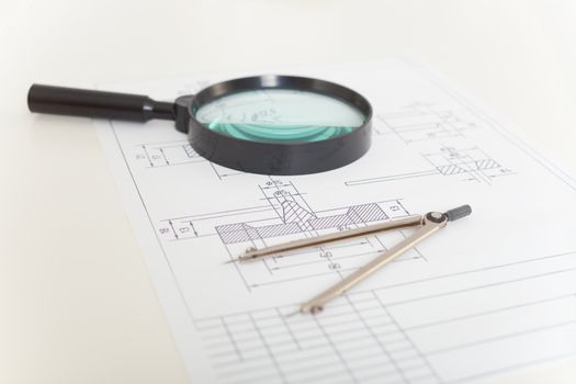 The drawings, magnifier and compasses on a white table