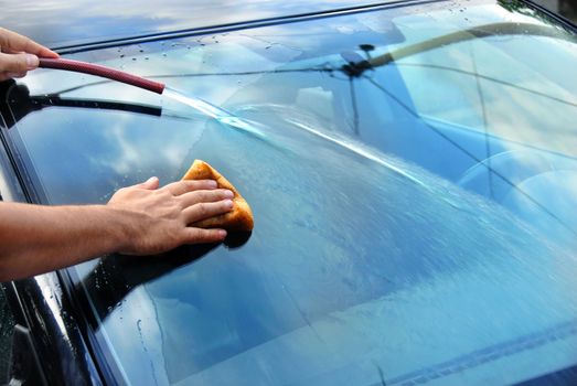 hands with hose and sponge washing blue car glass