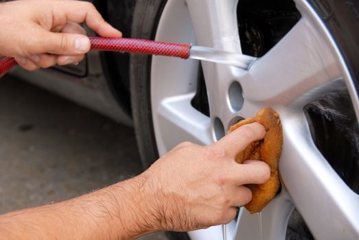 hands with hose and sponge washing blue car glass