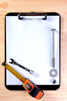 Office accessories for information preservation: Blank Clipboard for the worker with tape measure, wrench and bolt.