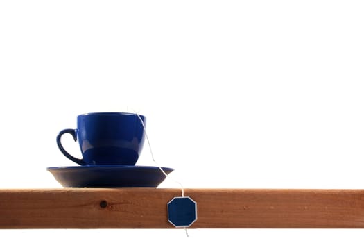 Dark blue tea cup with a saucer on a wooden shelf.