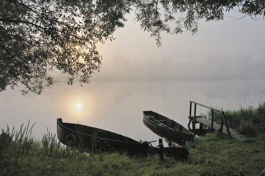 The sun, boats at coast in a morning fog rises.