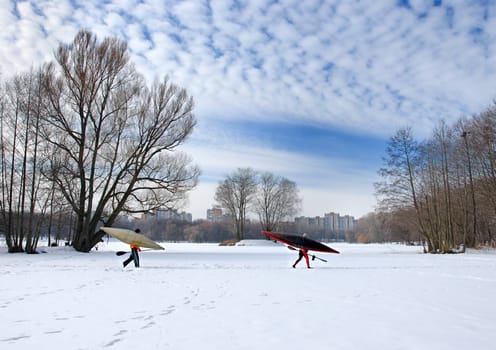 Two oarsmen with oars and kayaks go on ice of the frozen lake.