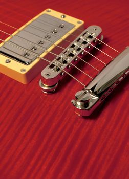 Closeup of red electric guitar showing pickup, bridge and detail of the wood grain.

