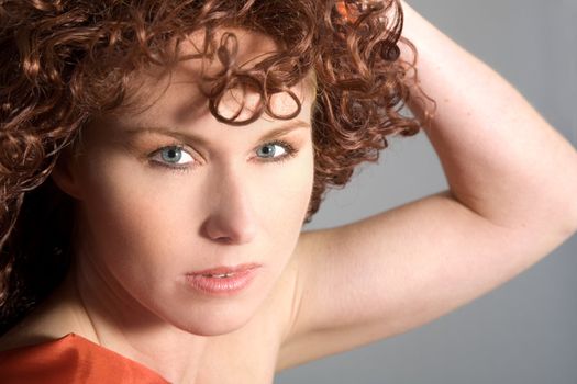 Beautiful girl with long red curls on grey background