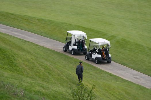Golf Course Out of Bounds is a capture of someone looking for their ball at the edge of the course with their golf carts parked on the path. 
