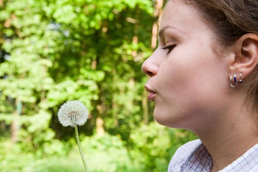 woman blowing the dandelion over the green forest background