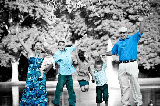 Portrait of a fun young family with four children jumping in the air all at once.  Selective isolated color highlighting the blues.