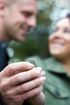 A young happy couple holding a diamond engagement ring.  Shallow depth of field with focus on the ring.