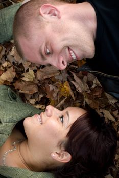 A young happy couple gazing into each others eyes while laying in a pile of leaves.