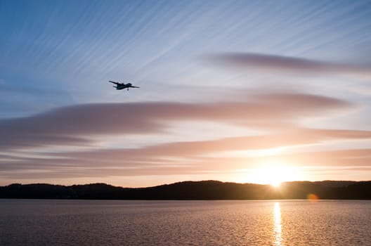 Airplane in the sunset over the water with blue sky and hills in the background