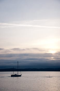 Sailboat in dark sunset with hills in the background