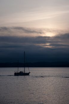 Sailboat in dark sunset with hills in the background