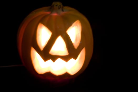 Halloween Pumpkin on a black background. The eyes nose and mouth are bright yellow from a light inside.